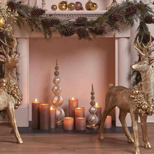 Decorative setup with gold deer, candles, and a garland on a fireplace.