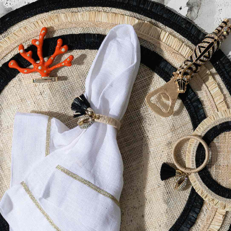 White napkin with a decorative ring on a woven mat with Coral-shaped place card holder in coral enamel with gold and crystal accents by Joanna Buchanan.