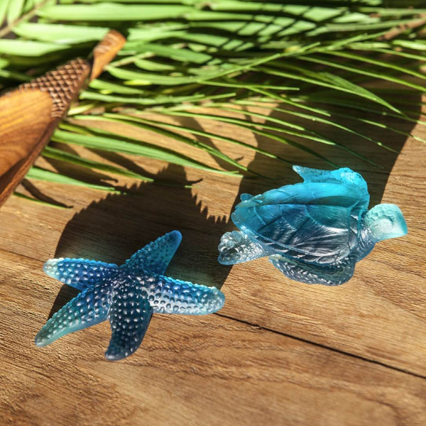 Blue sea turtle and starfish figurines on a wooden surface with palm leaves in the background