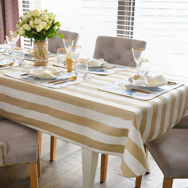 Dining table set with striped tablecloth, glasses, and flowers in a bright room.