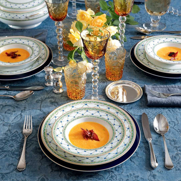Elegant table setting with soup, cutlery, and colorful glasses on a blue tablecloth.