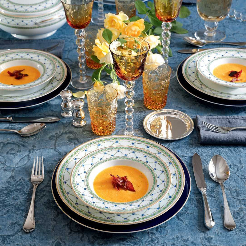 Elegant table setting with soup, cutlery, and colorful glasses on a blue tablecloth.