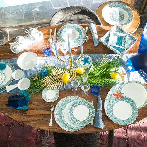 Dining table set with decorative plates from Portofino collection, glasses, and a centerpiece on a wooden table.