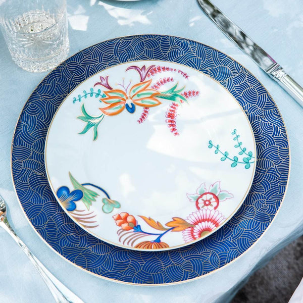 Decorative plate with floral design on a blue patterned rim, placed on a light blue table.