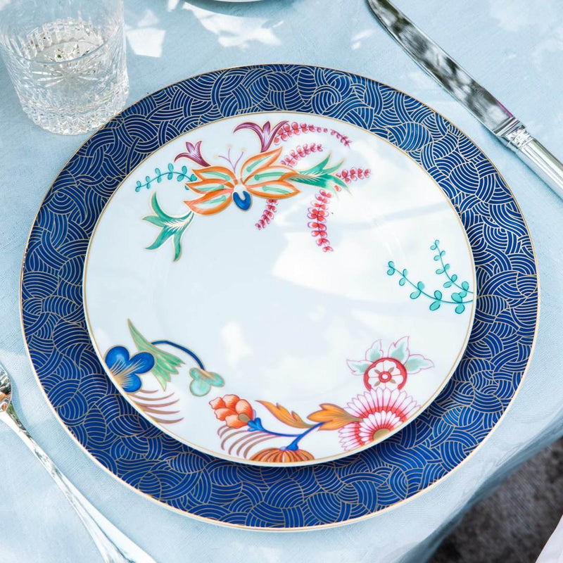 Decorative plate with floral design on a blue patterned rim, placed on a light blue table.