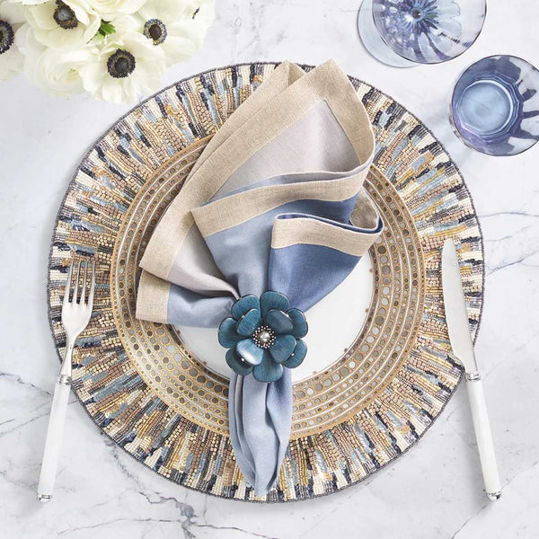 Decorative placemat with a patterned edge, folded napkin, and floral napkin ring on a marble surface.