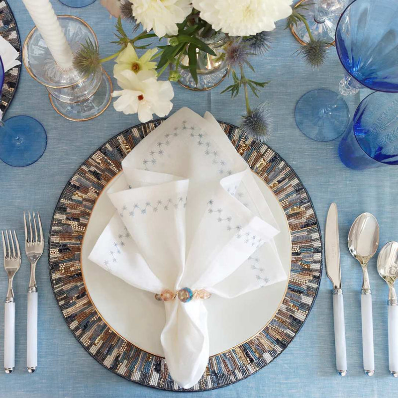 Elegant table setting with decorative plates, white napkins, and silverware on a blue tablecloth.