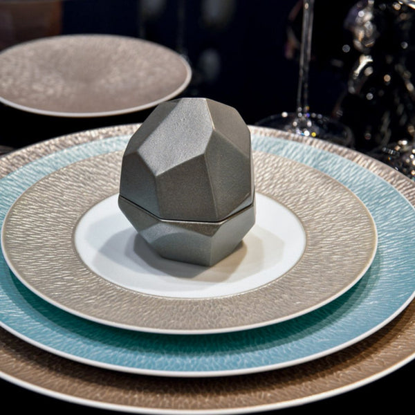 Geometric gray object on a stack of ceramic plates with a blurred background