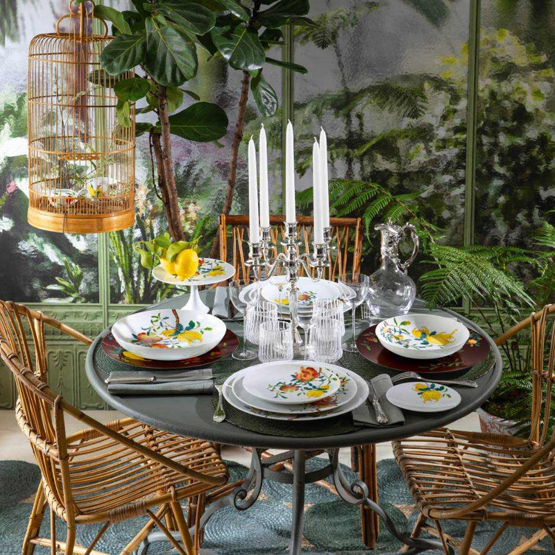 Dining table set with floral dinner plates Harmonia, glasses, and cutlery in a stylish room with plants and decor.