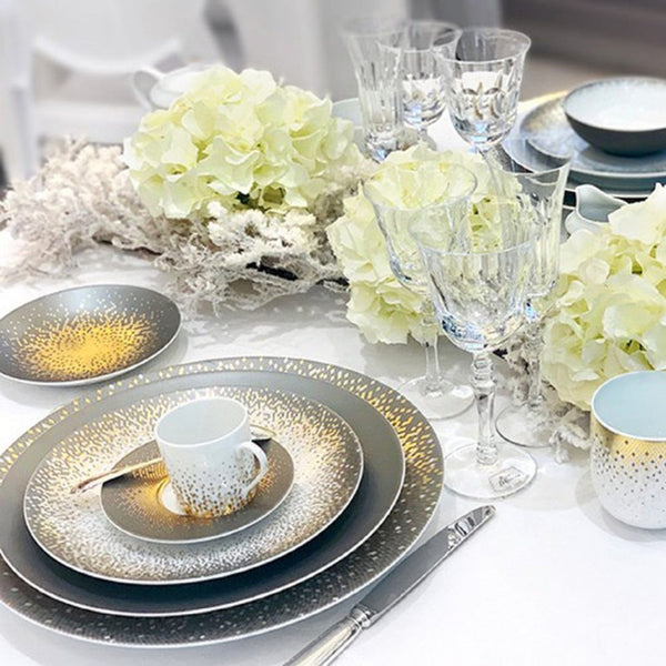 Elegant table setting with gold and silver plates, white flowers, and crystal glasses.