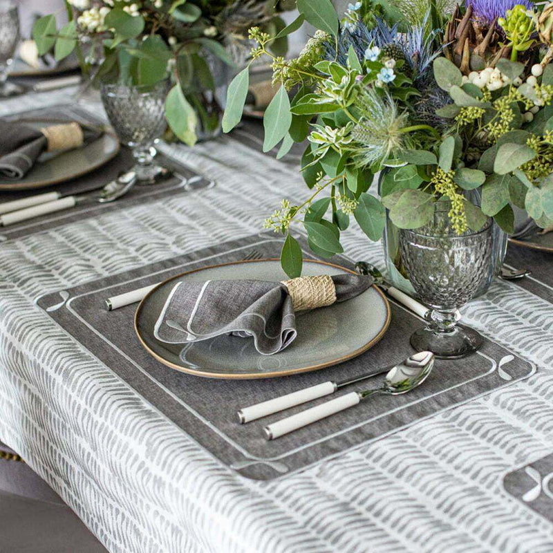 Elegant table setting with gray plates, napkins, and silverware on a patterned tablecloth.