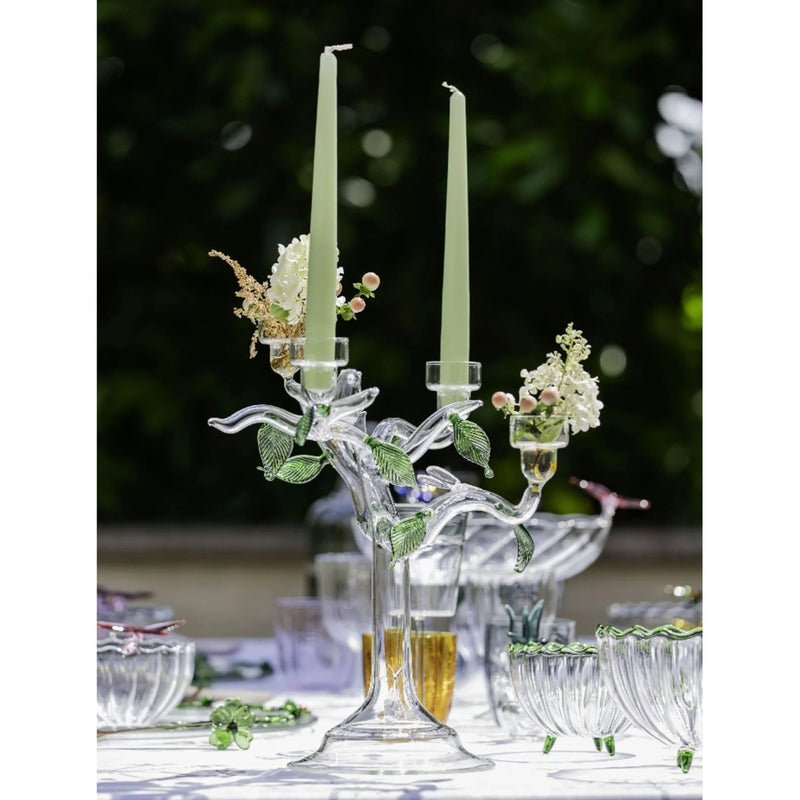 Decorative glass candelabra with candles and flowers on a table setting outdoors.