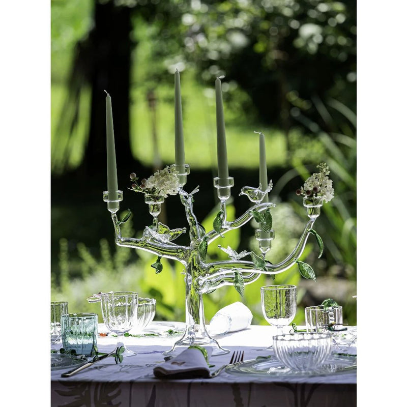 Decorative glass candelabra on a table with greenery in the background