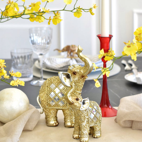 Decorative gold elephant figurine on a table with yellow flowers and a red candle holder.