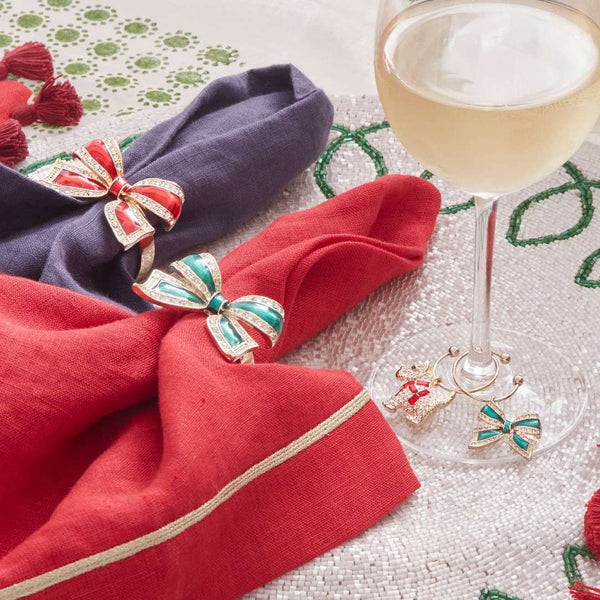 Decorative napkin rings with bow designs on folded napkins next to a glass of white wine.