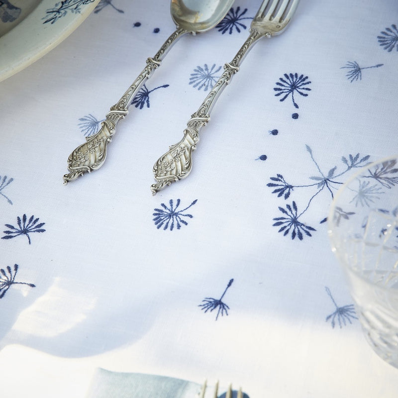 close-up of white linen tablecloth with embroidered blue flowers and styled with silveware