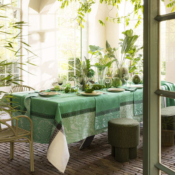 Dining table set with green tablecloth and decor in a bright room with plants
