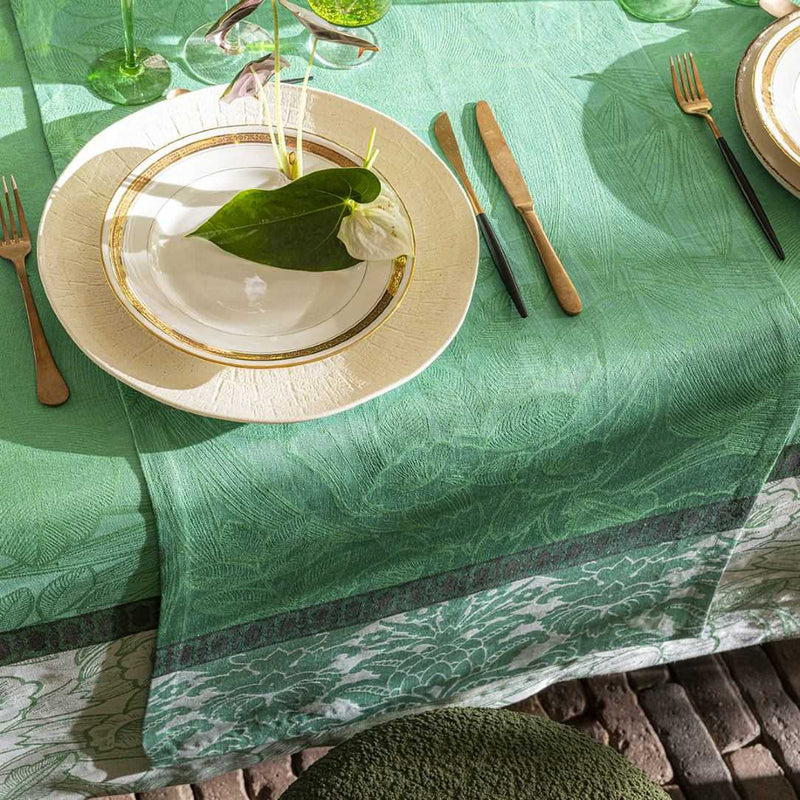 Dining table setting with green tablecloth, plates, cutlery, and leaves.