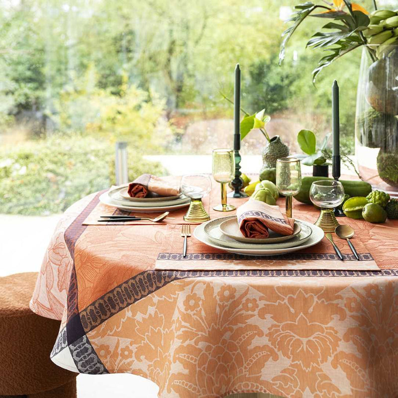 Dining table set with plates, glasses, and cutlery on a patterned tablecloth with a garden view.