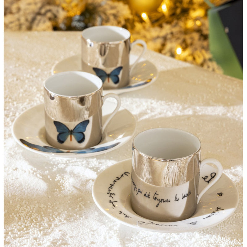 Porcelain cups with butterfly design on saucers against a blurred decorative background
