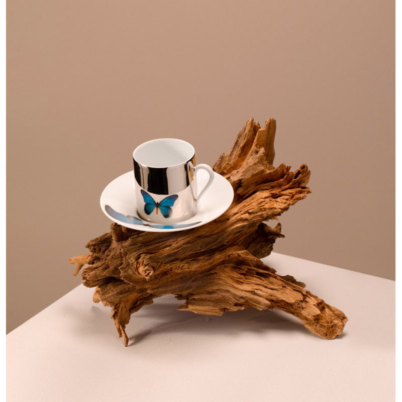 Porcelain cup & saucer with butterfly design on a saucer placed on a piece of driftwood against a beige background