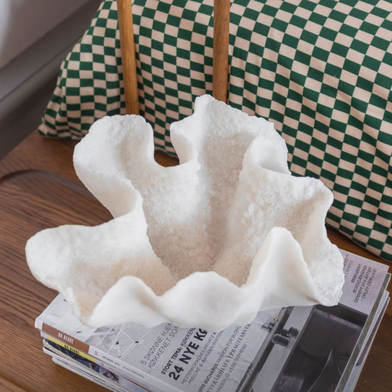 Decorative coral-like object on a stack of newspapers with a checkered chair in the background