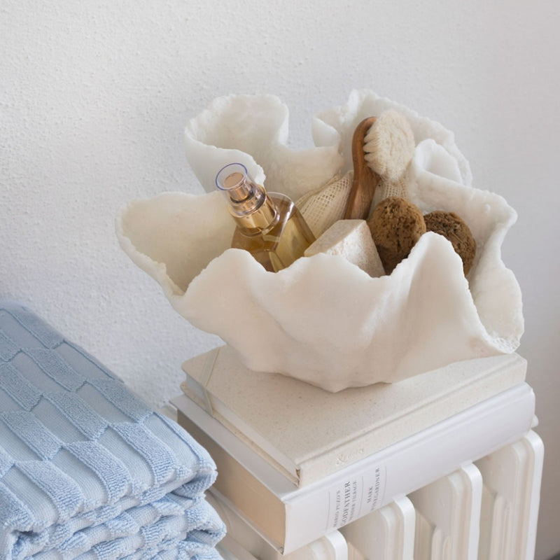 White faux shell bowl with bath items on a white surface
