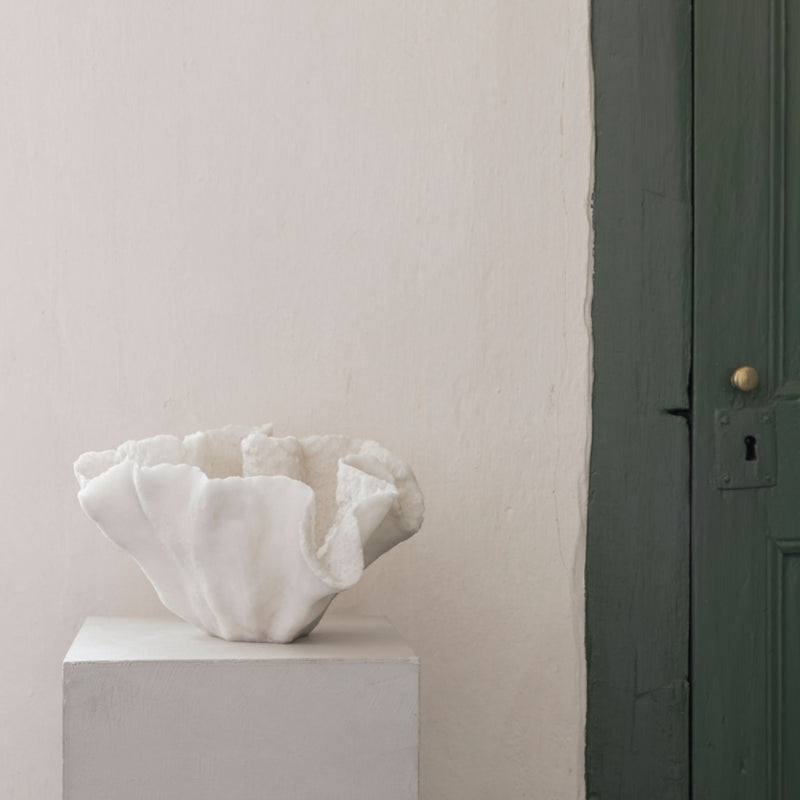 White faux shell decor bowl on a pedestal against a light pink wall with a dark green door.