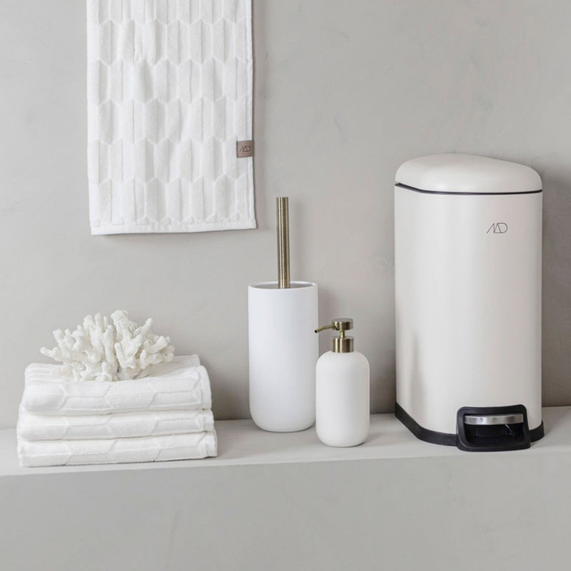 White bathroom accessories including a trash can, soap dispenser, and bath towels on a gray surface.