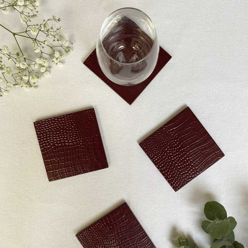 Brown crocodile-patterned coasters with a glass of water on a white surface.