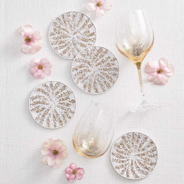 Decorative glassware with gold patterns coasters and pink flowers on a light background