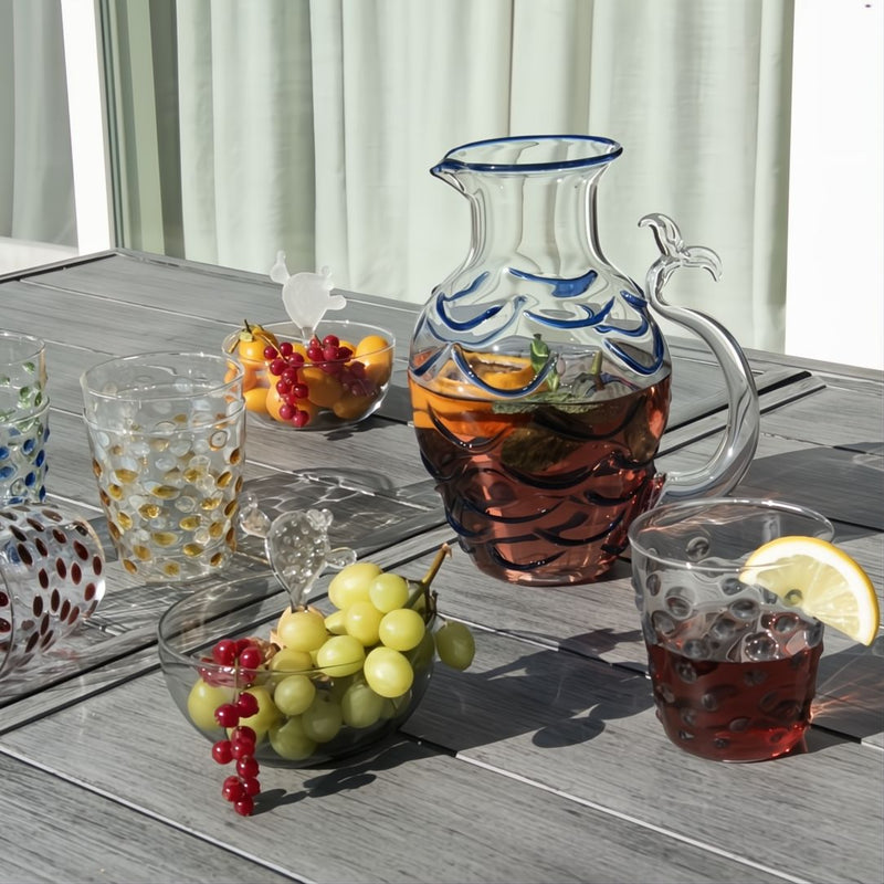 Outdoor setting with a fish tail glass pitcher of iced tea, glasses, and fruit on a wooden table.