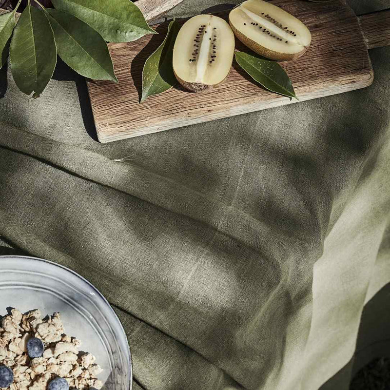 Sliced kiwi on a wooden cutting board with green leaves on a textured surface