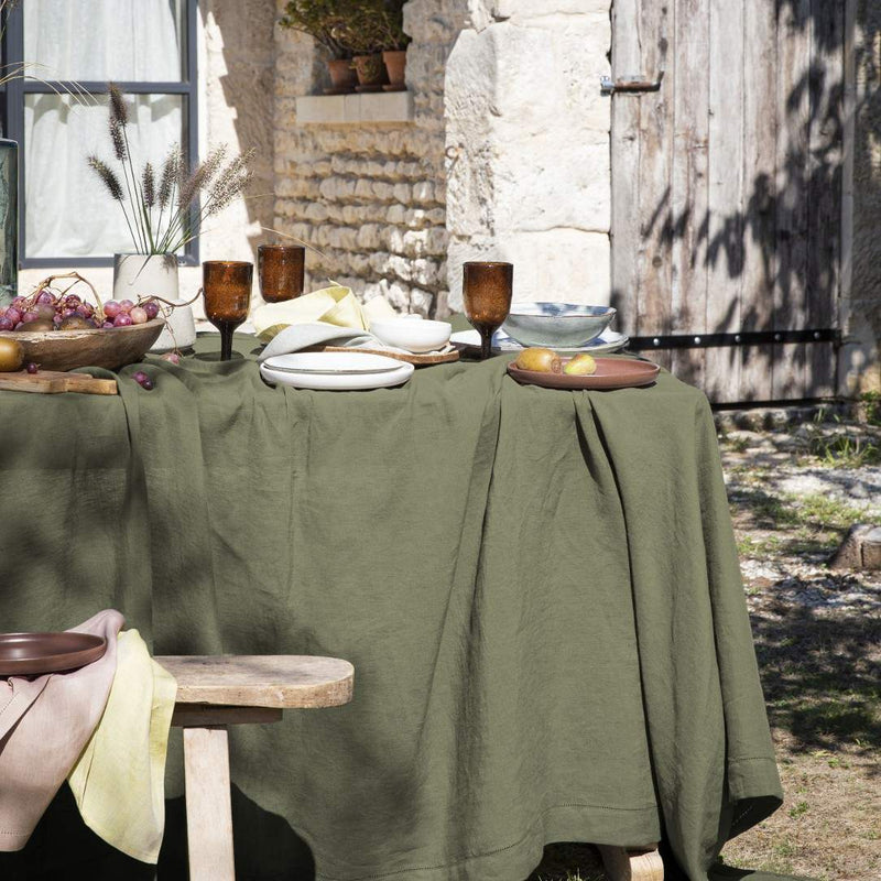 Outdoor setting with a table draped in a green tablecloth, set with plates and glasses.
