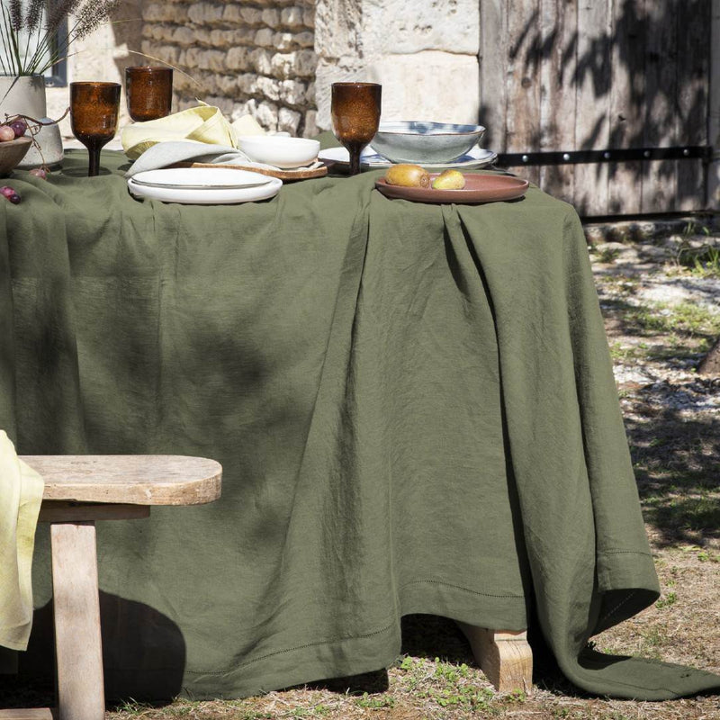 Green tablecloth on a table outdoors with stone wall and wooden bench in the background