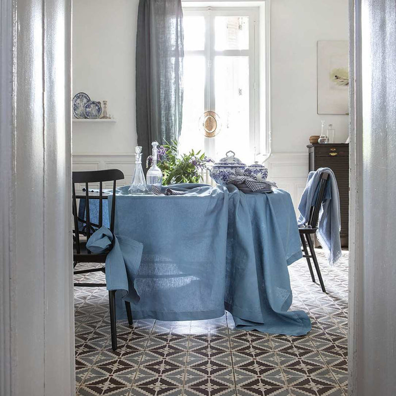 Dining room with a table covered in a blue cloth, chairs draped with blue cloths, and decorative items.