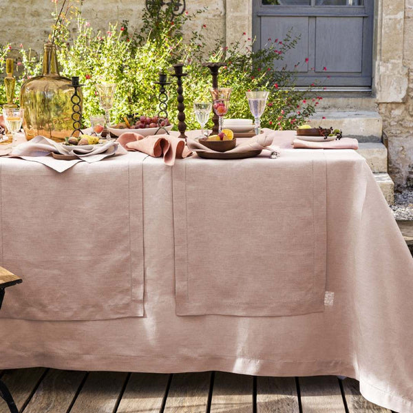 Dining table set with pink tablecloth, plates, glasses, and candles outdoors.