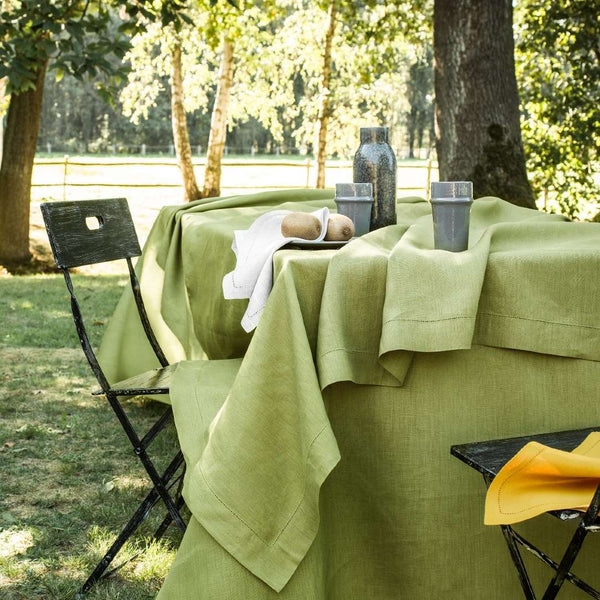 Green tablecloth on a table outdoors with chairs and a bottle.