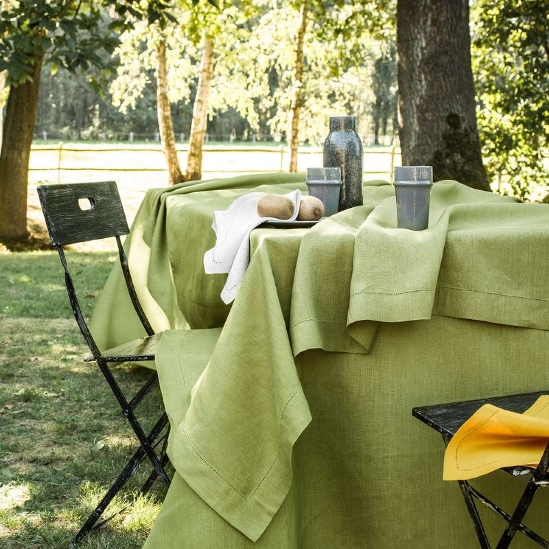 Green tablecloth on a table outdoors with chairs and a bottle.