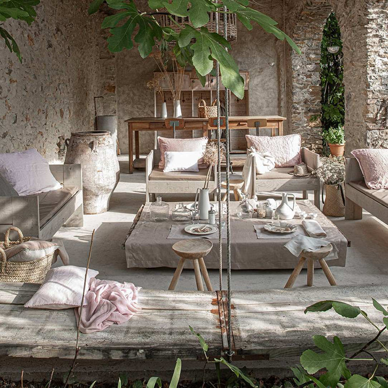Outdoor patio with wooden furniture, cushions, and a small table set for a meal.