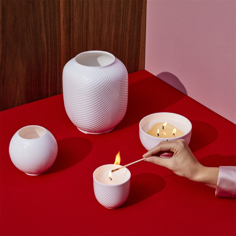 White ceramic vases on a red surface with a hand lighting a candle.