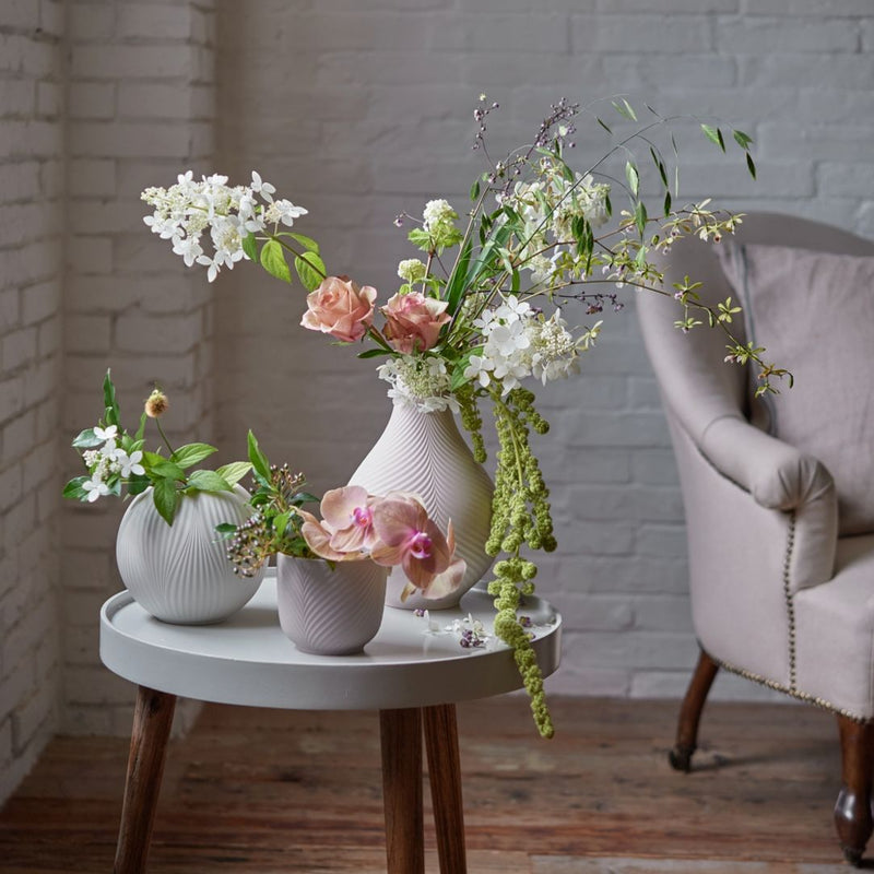Floral arrangements in white vases on a small round table against a brick wall.