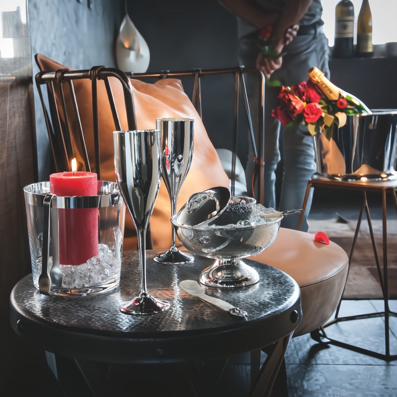 Decorative setting with wine glasses, a candle, and a Footed silver-plated caviar bowl by Sonja Quandt in a cozy room.