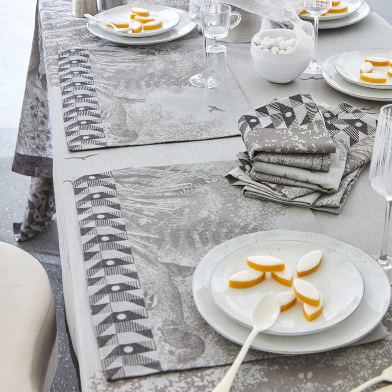 Dining table setting with patterned placemats and napkins on a light gray surface.