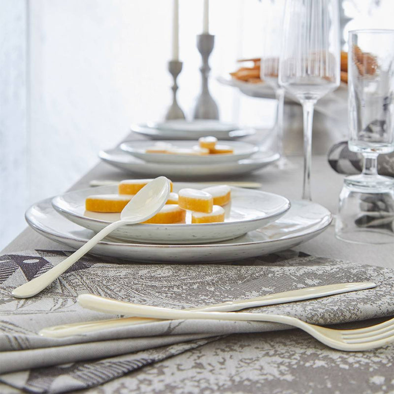 Dining table setting with plates, cutlery, and glasses on a patterned tablecloth.
