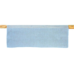 A light blue linen table runner is displayed on a wooden rod, showcasing its texture and color.
