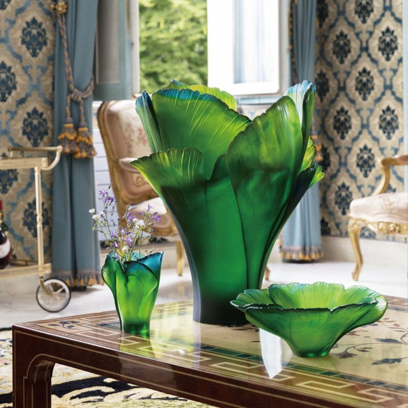Green glass vase and bowl on a table in an elegant room with patterned wallpaper and chairs.