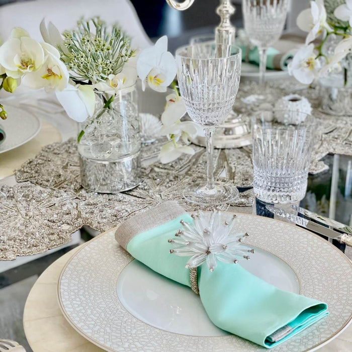 Elegant table setting with crystal glasses, white flowers, and a mint green napkin.
