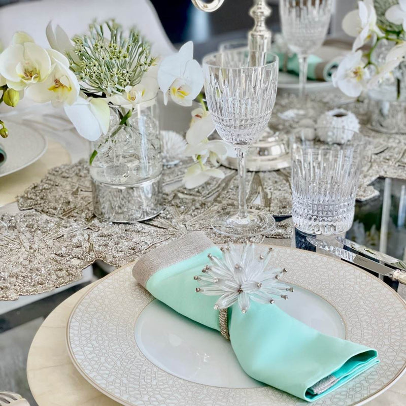 Elegant table setting with crystal glasses, white flowers, and a mint green napkin.