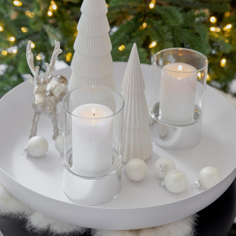 Decorative setup with candles, white ornaments, and Christmas trees on a table.